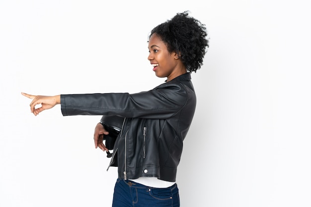 Młoda amerykanin afrykańskiego pochodzenia kobieta z hełma motocyklu na biel ścianie wskazuje palec z boku