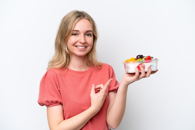 Zdjęcie młoda angielka trzyma miskę owoców na białym tle i wskazuje ją