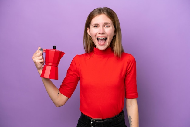 Młoda Angielka trzymająca dzbanek do kawy na fioletowym tle z zaskoczeniem i zszokowanym wyrazem twarzy