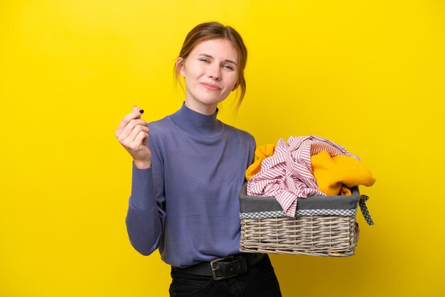 Młoda Angielka trzymająca kosz na ubrania na żółtym tle robiąca gest pieniędzy