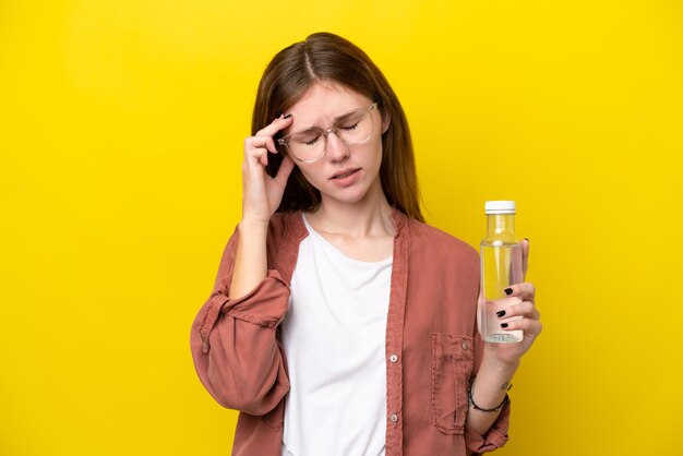 Młoda Angielka z butelką wody odizolowaną na żółtym tle z bólem głowy