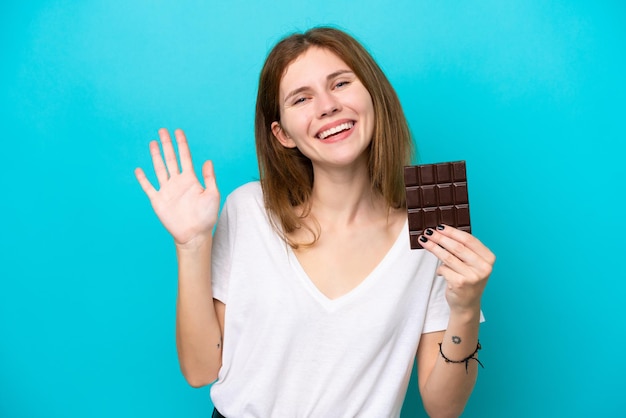 Młoda Angielka z czekoladą na białym tle pozdrawiająca ręką z radosnym wyrazem twarzy