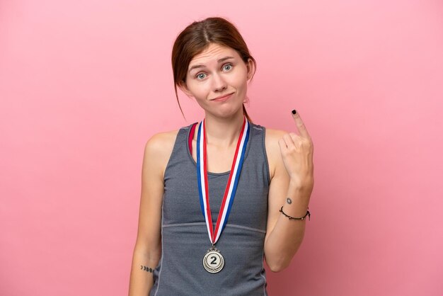 Zdjęcie młoda angielka z medalami na białym tle na różowym tle wskazująca palcem wskazującym to świetny pomysł