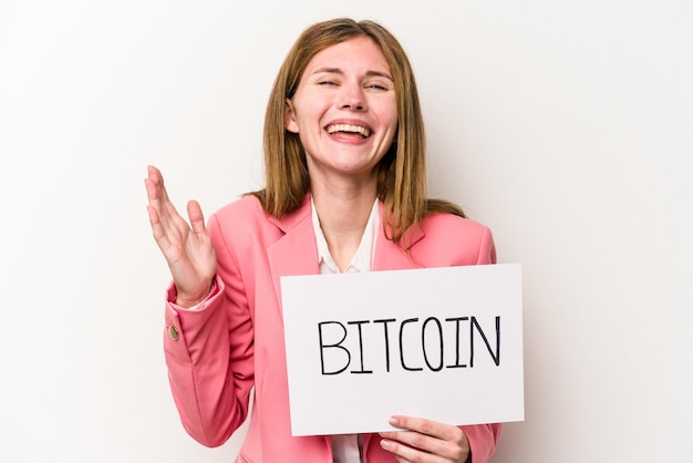 Młoda angielska kobieta biznesu trzymająca tabliczkę bitcoin na białym tle otrzymuje miłą niespodziankę podekscytowaną i podnoszącą ręce