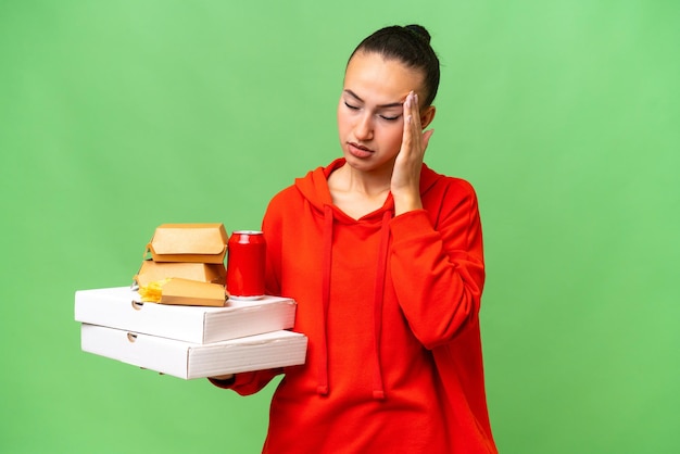 Młoda Arabka trzymająca fast food na odosobnionym tle z bólem głowy