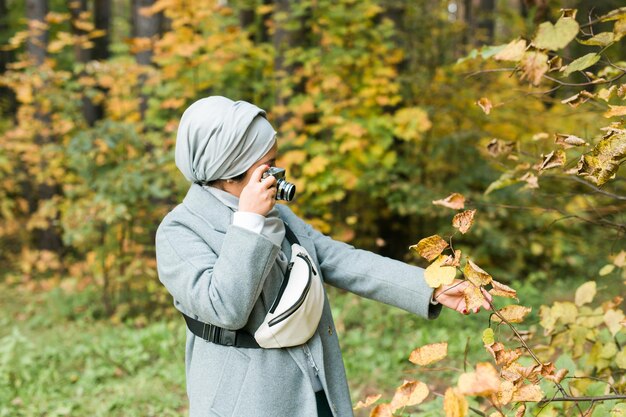 Młoda arabska kobieta nosząca hidżab chustę na głowie fotografująca smartfonem w parku nowoczesna muzułmańska dziewczyna