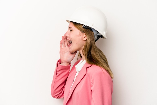 Zdjęcie młoda architektka angielka z hełmem na białym tle krzycząca i trzymająca dłoń w pobliżu otwartych ust