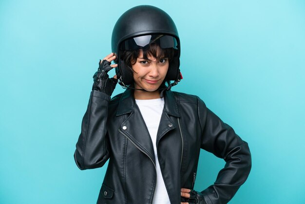 Młoda argentyńska kobieta w kasku motocyklowym na białym tle na niebieskim tle ma wątpliwości