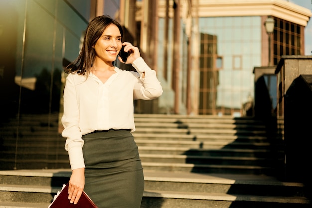 Młoda atrakcyjna biznesowa kobieta w bluzce i spódnicy rozmawia przez telefon. Pomysł na biznes