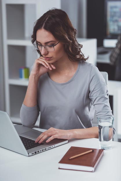 Młoda atrakcyjna bizneswoman w zwykłych ubraniach przy użyciu laptopa podczas pracy w biurze