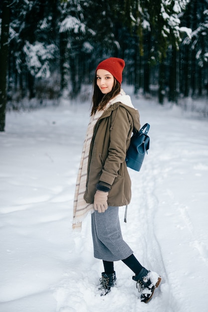 Młoda atrakcyjna brunetka dziewczyna z ciepłym szalikiem i czerwonym kapeluszem, pozowanie w lesie śniegu
