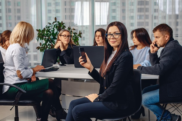 Młoda atrakcyjna dziewczyna o ciemnych włosach, ubrana w kurtkę, siedząca w swoim miejscu pracy w biurze