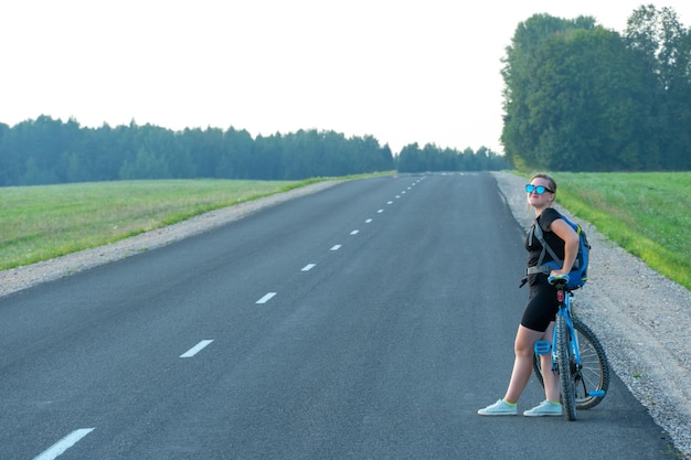 Młoda Atrakcyjna Dziewczyna Stoi Na Utwardzonej Drodze Obok Swojego Roweru Jazda Na Rowerze Po Okolicy Jazda Na Rowerze Jako Sposób Na Spędzanie Czasu I Zdrowy Styl życia