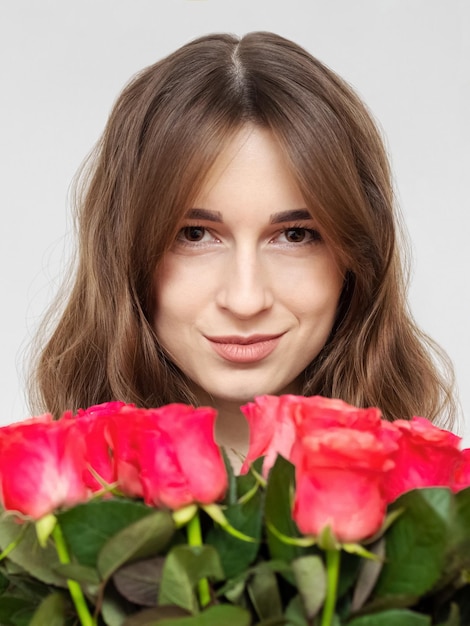 Młoda atrakcyjna dziewczyna z bukietem czerwonych róż na białym tle z bliska Szczęśliwa dziewczyna z bukietem róż się uśmiecha Koncepcja szczęścia, radości i świętowania