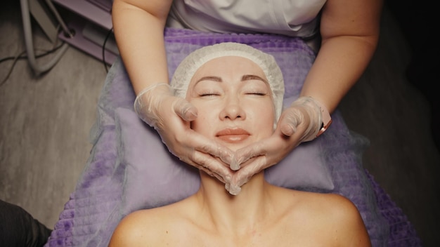 Młoda atrakcyjna kobieta kaukaski odbiera anti-aging masaż twarzy w salonie spa relaks na stole do masażu. Wellness pielęgnacja ciała i skóry, pielęgnacja twarzy, zabieg odmładzania