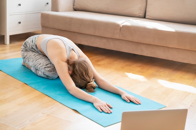 Młoda Atrakcyjna Kobieta Robi ćwiczenia Jogi W Domu, Balasana, Dziecko Stanowią, Ardha-kurmasana Pół żółwia Stanowią W Salonie. ćwiczenie Noszenia Stanika I Spodni Sportowych. Pojęcie Opieki Zdrowotnej