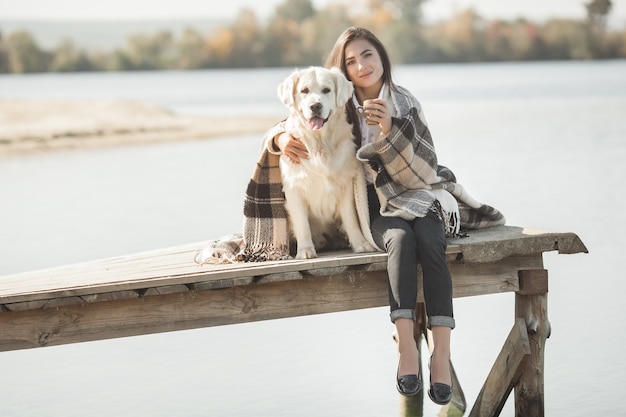 Młoda atrakcyjna kobieta siedzi na molo z psem. Najlepsi przyjaciele na zewnątrz