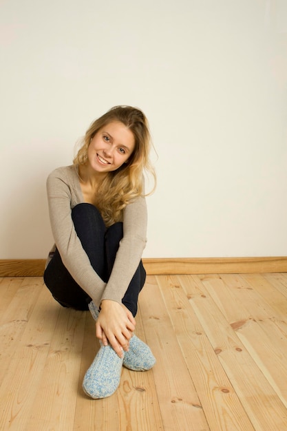 Zdjęcie młoda atrakcyjna kobieta siedzi w domu na drewnianej podłodze ze skrzyżowanymi nogami