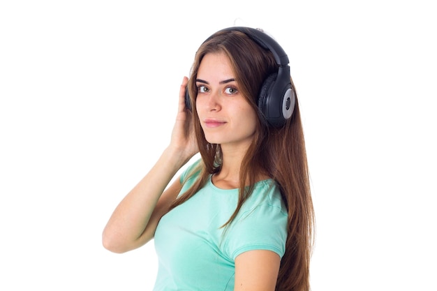 Młoda atrakcyjna kobieta w niebieskiej koszulce i czarnych słuchawkach na białym tle w studio