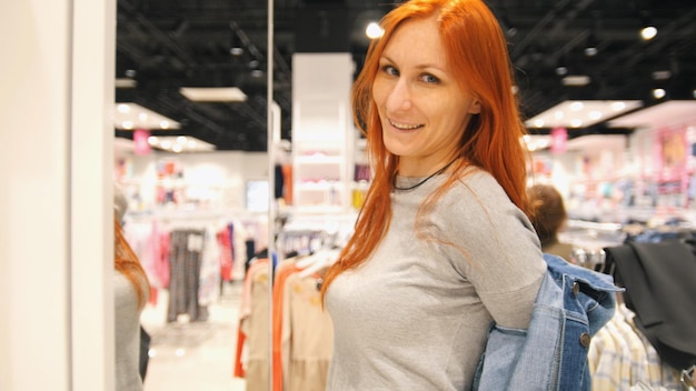Młoda atrakcyjna kobieta wybiera kurtkę jeansową w sklepie z odzieżą damską, z bliska
