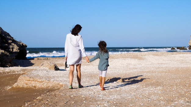 Zdjęcie młoda atrakcyjna kobieta z małą córeczką idzie razem na plaży, widok z tyłu.