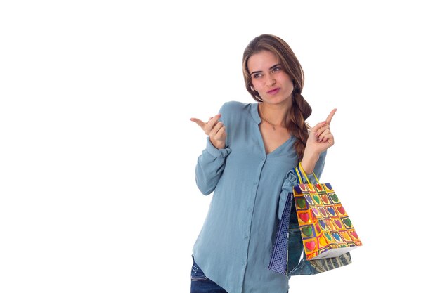 Młoda atrakcyjna kobieta z warkoczem w niebieskiej bluzce trzymająca różnokolorowe torby na zakupy w studio