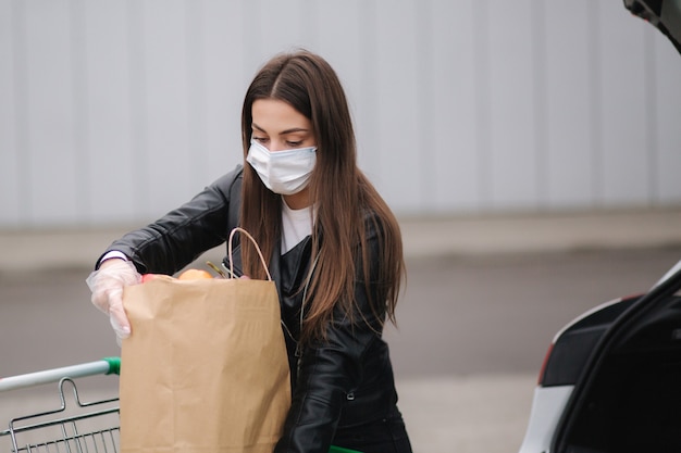 Młoda atrakcyjna kobieta zabiera artykuły spożywcze z supermarketu z wózka do samochodu