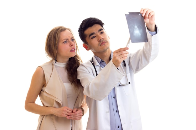 Młoda atrakcyjna lekarka z czarnymi włosami w sukni ze stetoskopem pokazująca Xray młodej smutnej kobiecie