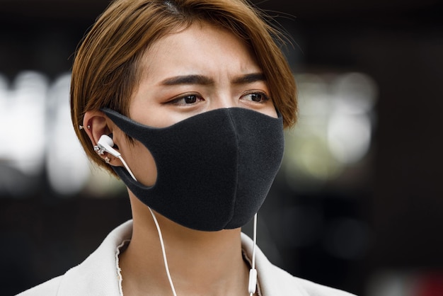 Młoda Azjatka nosząca maskę na zewnątrz podczas słuchania muzyki w mieście podczas pandemii COVID19