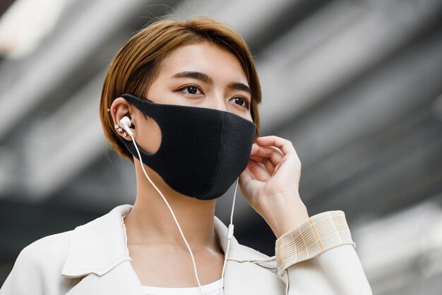 Młoda Azjatka nosząca maskę na zewnątrz podczas słuchania muzyki w mieście podczas pandemii COVID19