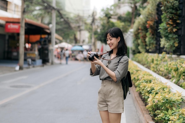 Młoda Azjatka podróżująca z plecakiem za pomocą cyfrowego aparatu kompaktowego, ciesząca się lokalnym kulturowym miejscem i uśmiechem Podróżnik sprawdzający boczne ulice