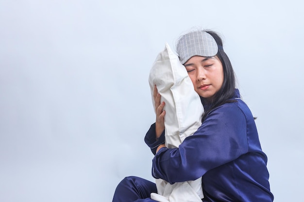 Młoda Azjatka śpiąca w piżamie i masce do oczu podczas trzymania i przytłaczania poduszki