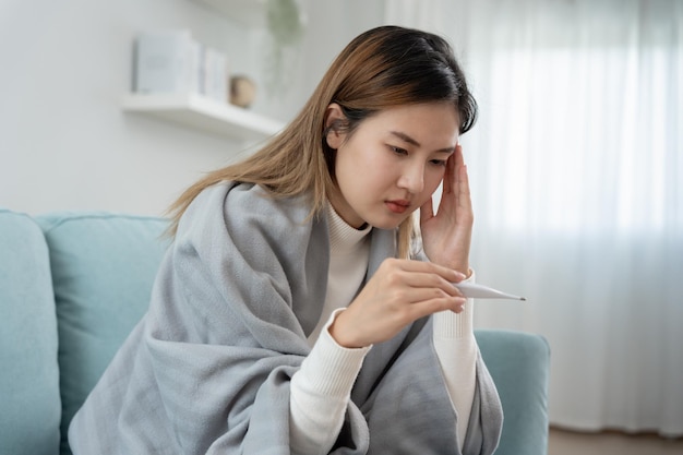Młoda Azjatka z wysoką gorączką podczas sprawdzania temperatury ciała kobieta kichająca i cieknąca z nosa z sezonową grypą alergiczny termometr cyfrowy wirus koronawirusa choroba układu oddechowego