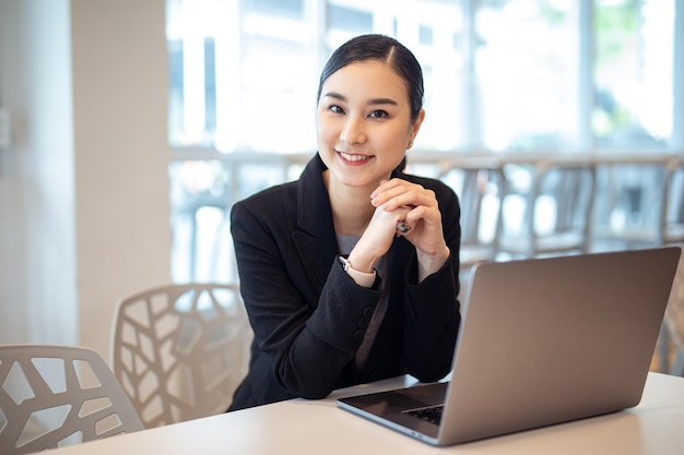 Młoda azjatycka biznesowa dziewczyna pracuje z laptopem w biurze uśmiechnięty aparat fotograficzny