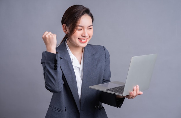 Młoda azjatycka biznesowa kobieta ubrana w garnitur i korzystająca z laptopa na szarym tle