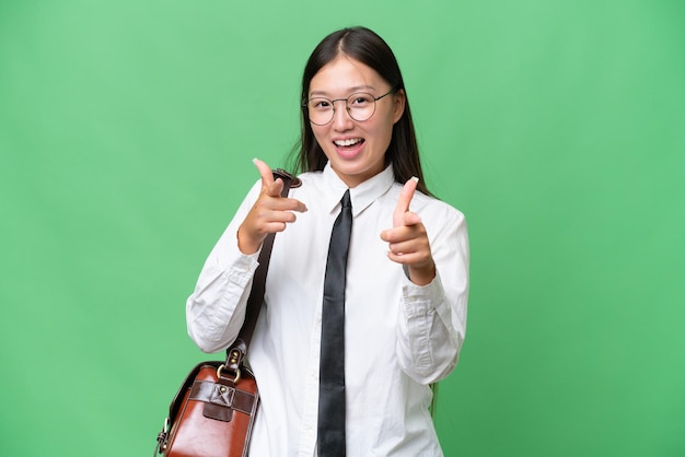 Młoda azjatycka biznesowa kobieta wskazuje na przód i uśmiecha się na odosobnionym tle