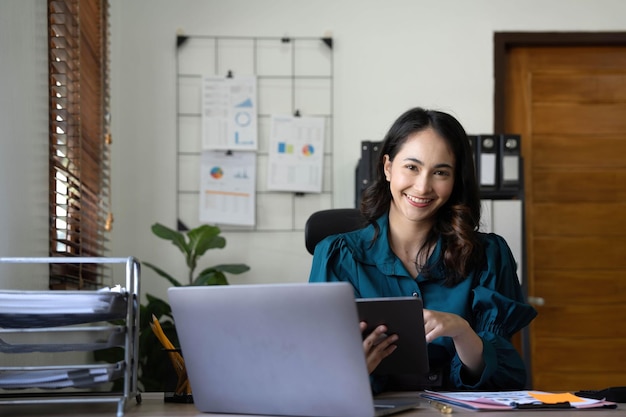 Młoda azjatycka bizneswoman pracuje na tablecie z laptopem w biurze