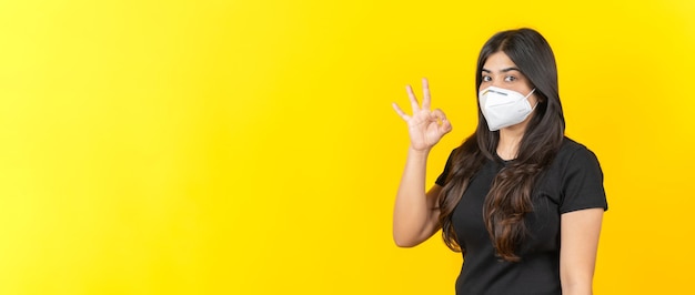 Młoda Azjatycka dziewczyna nosząca medyczną maskę na twarz w swobodnym ubraniu na żółtym tle