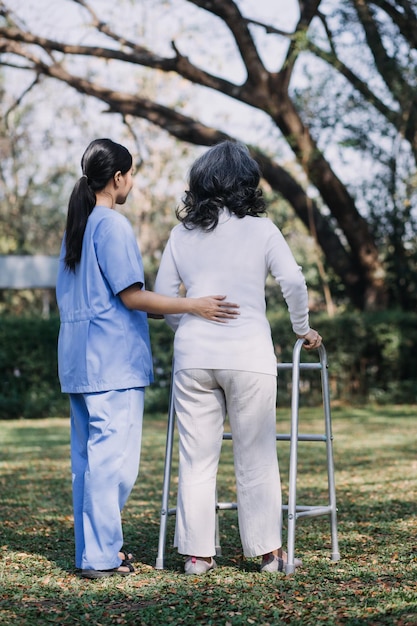 Młoda azjatycka fizjoterapeuta pracująca ze starszą kobietą podczas chodzenia z chodzikiem