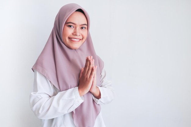 Młoda azjatycka islamska kobieta nosząca chustę podaje powitanie z wielkim uśmiechem na twarzy Indonezyjska kobieta na szarym tle Pozdrowienie Eid Mubarak