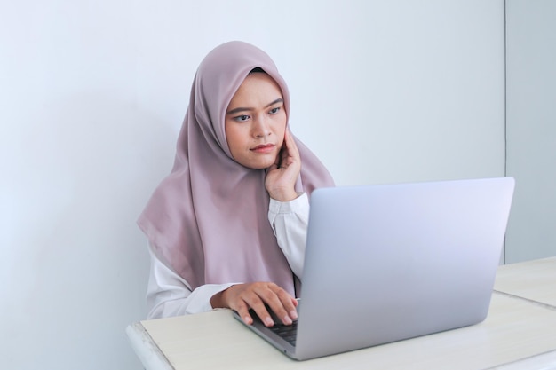 Młoda Azjatycka Islamska kobieta nosząca chustę przykłada palec w policzek myśląc i patrząc w górę, żeby skopiować przestrzeń Udana Islam Indonezyjska kobieta na szarym tle