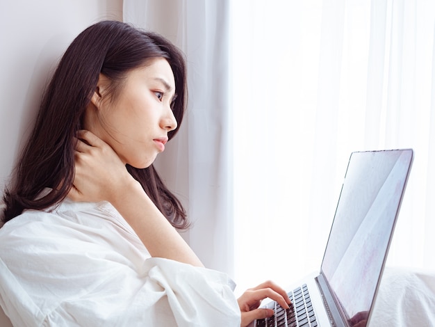 Młoda azjatycka kobieta cierpiąca na ból w ramieniu podczas korzystania z laptopa