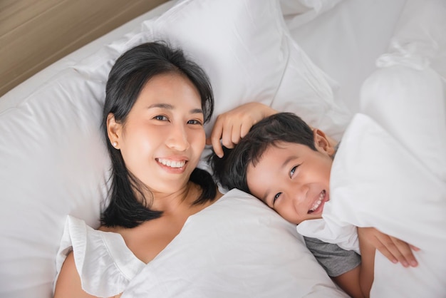 Młoda Azjatycka kobieta i syn śpią w swoim łóżku i relaksują się w sypialni, leżą na boku i relaksują się z zamkniętymi oczami, patrząc w kamerę
