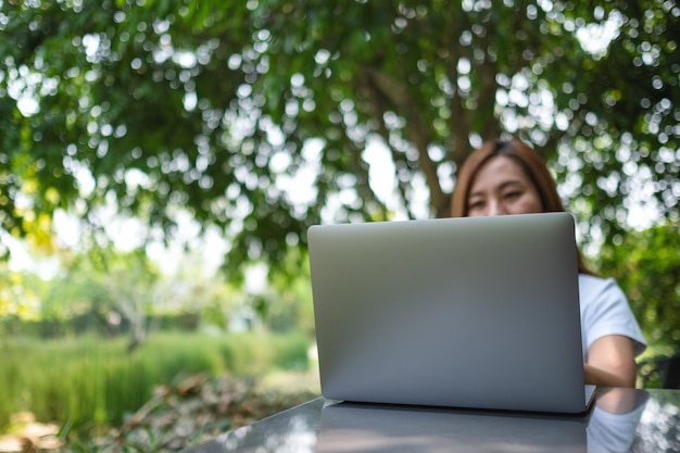 Młoda azjatycka kobieta korzystająca z laptopa i pracująca na nim siedząc w parku