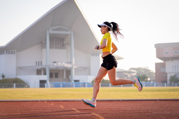 Młoda azjatycka kobieta lekkoatletka biegacza jogging na bieżni na stadionie miejskim w słoneczny poranek, aby zachować kondycję i zdrowy styl życia. Młoda kobieta fitness działa na torze stadionu. Sport i rekreacja