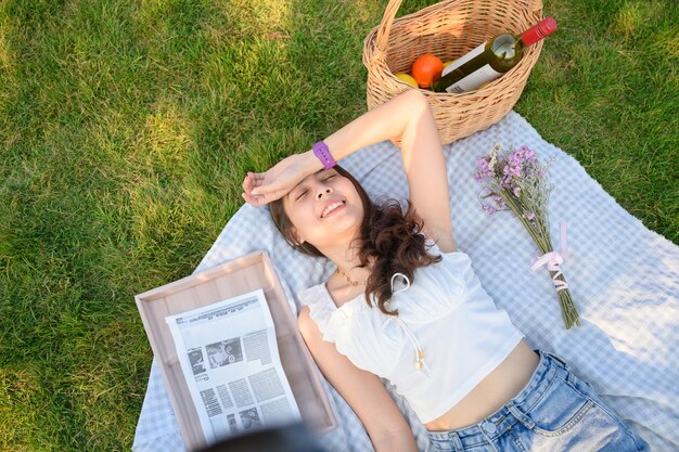 Młoda azjatycka kobieta leżąca na pikniku z wyposażeniem na trawie w słoneczny dzień