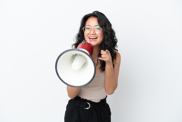 Młoda azjatycka kobieta na białym tle krzyczy przez megafon, aby ogłosić coś, wskazując jednocześnie na przód