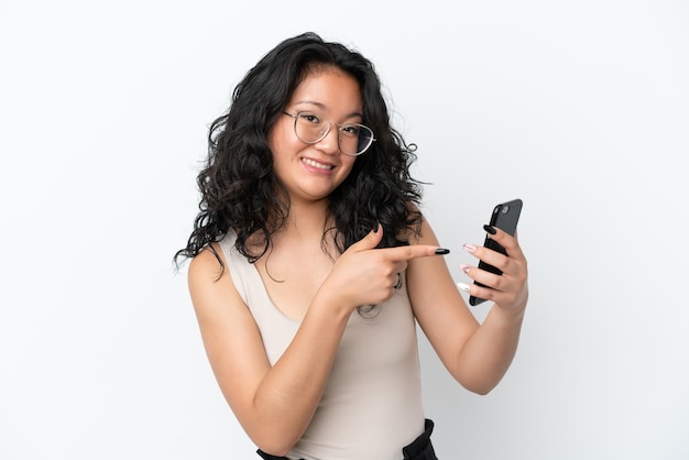 Młoda azjatycka kobieta na białym tle za pomocą telefonu komórkowego i wskazując go