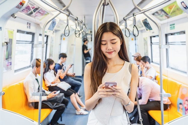 Młoda Azjatycka kobieta pasażera korzystająca z sieci społecznościowej za pośrednictwem inteligentnego telefonu komórkowego w pociągu metra