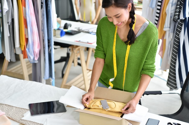 Młoda Azjatycka kobieta przedsiębiorca / projektant mody pracuje w studiu, pakuje i wysyła produkt